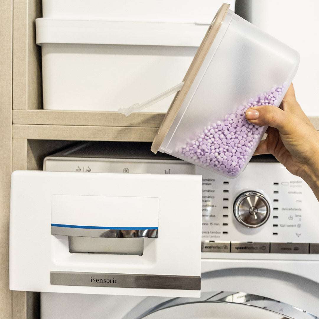 Cena de utilização da VRT Mini em contexto de lavandaria, com perolas perfumadas para a roupa, com máquina de lavar roupa e estante com as caixas Deco