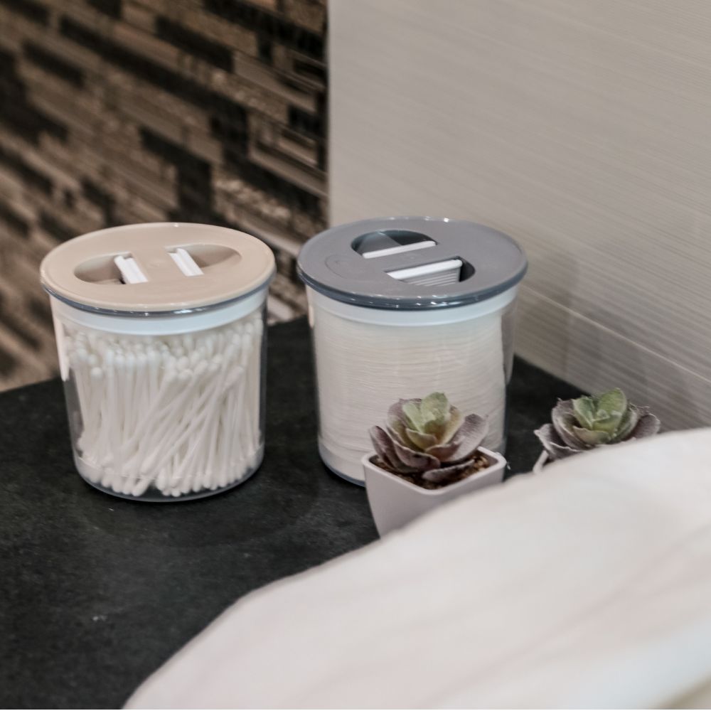 Duas herméticas com produtos de WC - cotonetes e discos de limpeza em balcão de WC.