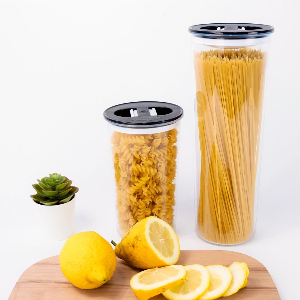 Conjunto de duas herméticas em ambiente de cozinha, com tábua de corte de madeira, com limões cortados. Recipientes com massas.