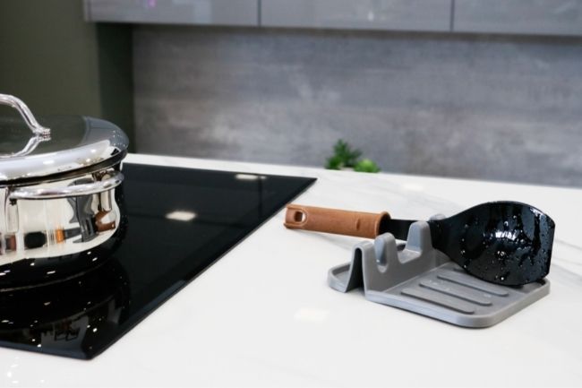 Suporte para utensilios, em bancada de cozinha junto a uma placa de indução, com uma colher