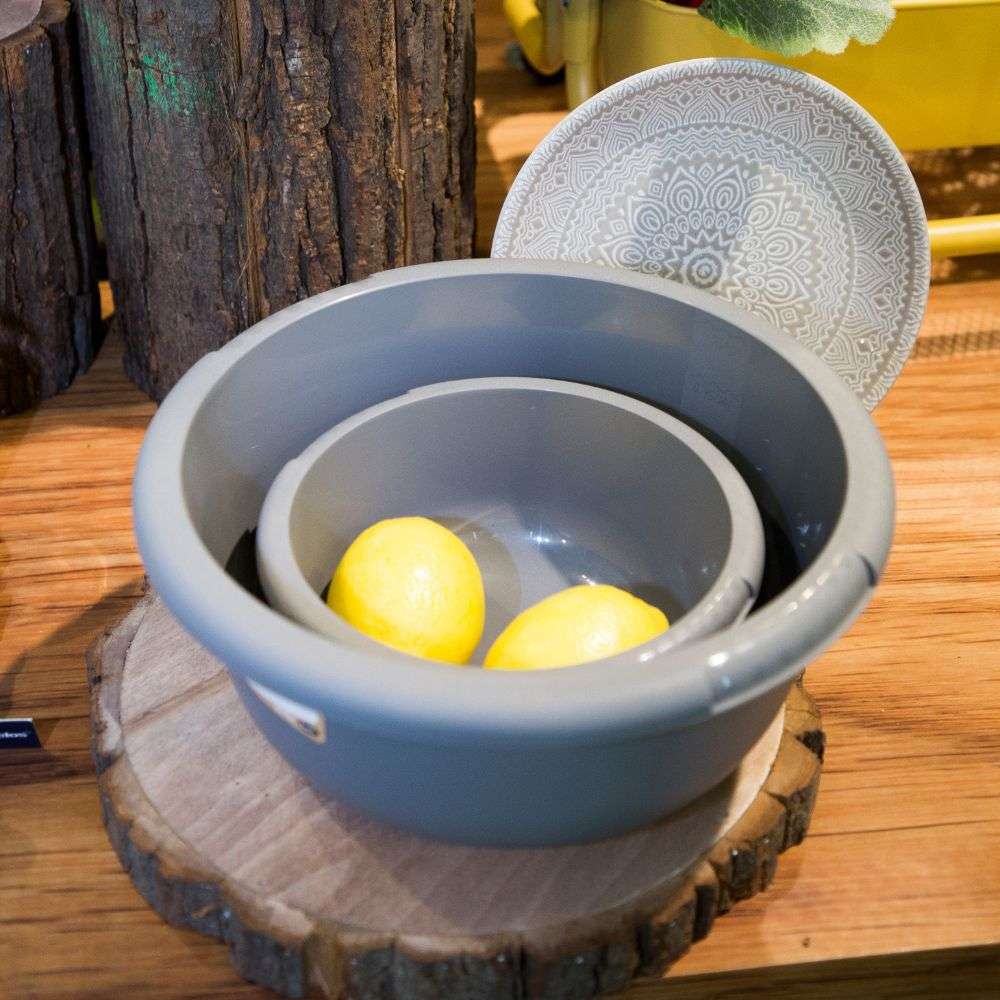 2 bacias de dois tamanhos diferentes, uma dentro da outra, com dois limões dentro da menor. Em cinzento. Fundo de madeira, com um prato por detrás e dois troncos de arvore