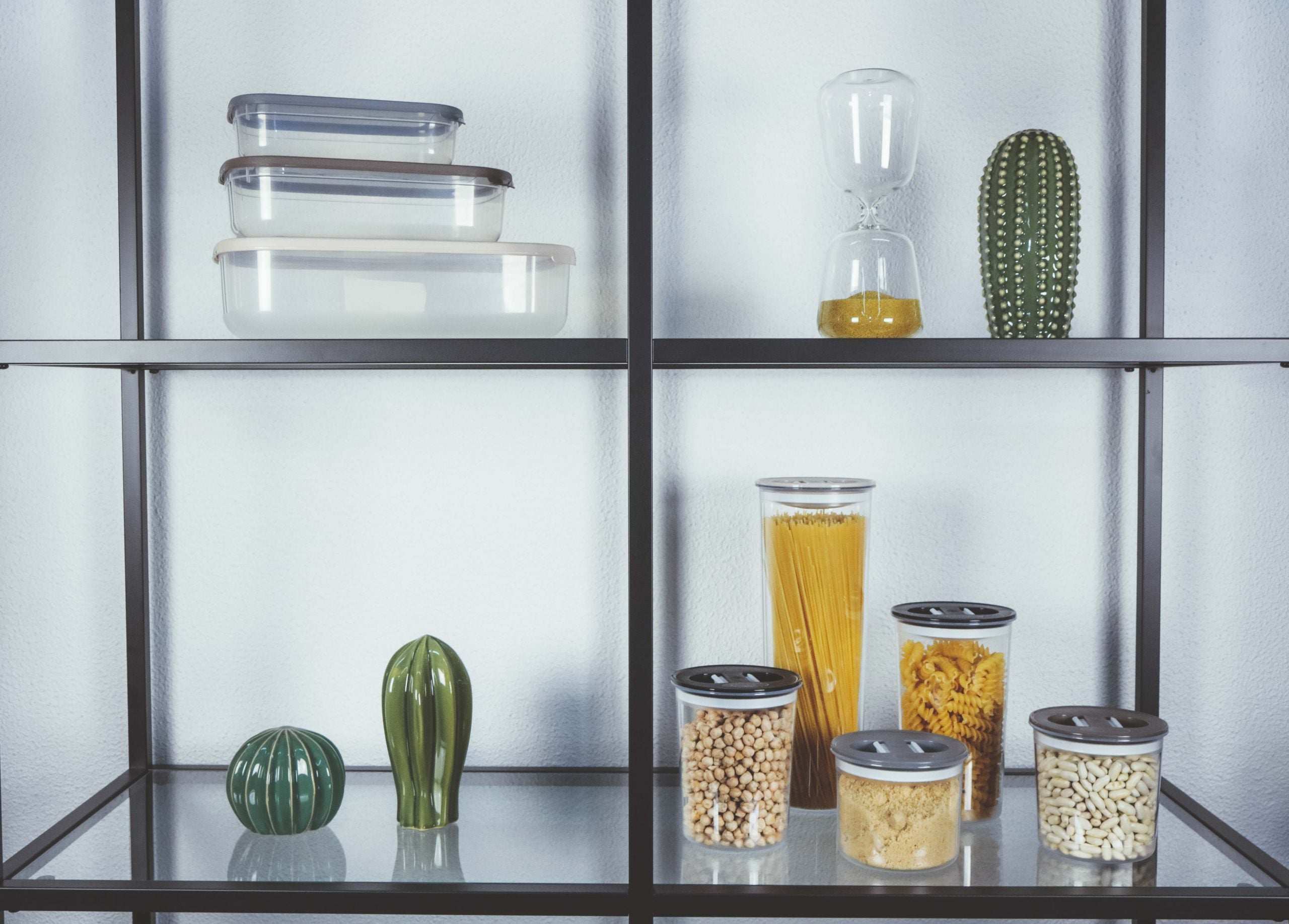 Conjunto de recipientes herméticos com alimentos secos dentro, numa estante com elementos de decoração. Contem conjunto de 3 recipientes para alimentos