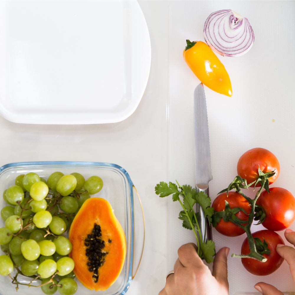 Recipiente para alimentos em vidro (Pyrex) com base em vidro e tampa em plástico flexivel branco. Foto de contexto, com legumes e frutos em ambiente de cozinha